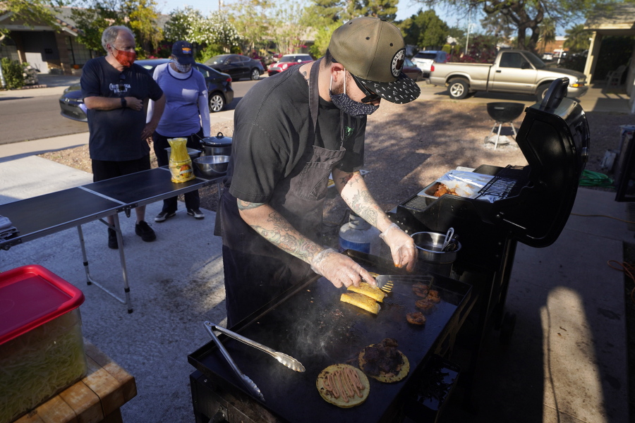 Chef Mike Winneker prepares tacos in front of his home Saturday, April 3, 2021, in Scottsdale, Ariz. Beaten down by the pandemic, many laid-off or idle restaurant workers have pivoted to dishing out food with a taste of home. Some have found their entrepreneurial side, slinging their culinary creations from their own kitchens. (AP Photo/Ross D.