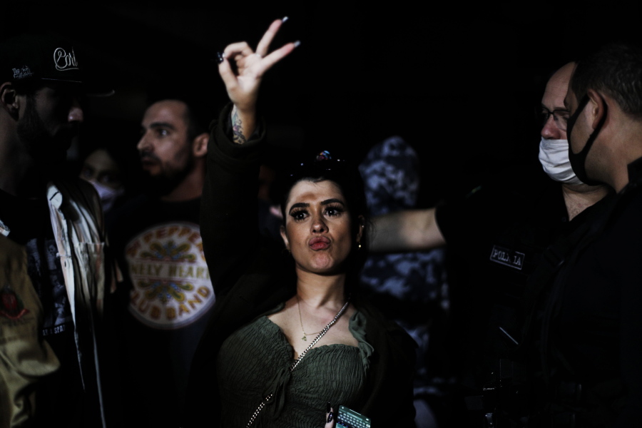 A woman flashes a V sign as police break up a social gathering during an operation against illegal and clandestine gatherings that authorities believe are partly responsible for fueling the spread of COVID-19, at a party hall in Sao Paulo, Brazil, early Saturday, April 17, 2021.