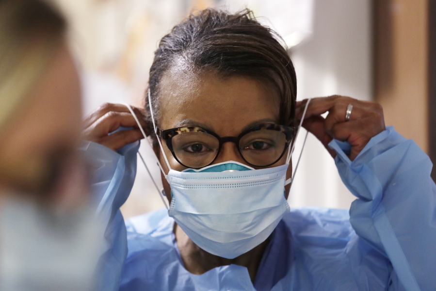 FILE - In this Friday, May 8, 2020 file photo, a respiratory therapist pulls on a second mask over her N95 mask before adding a face shield as she gets ready to go into a patient's room in the COVID-19 Intensive Care Unit at a hospital in Seattle.  Medical providers may soon return to using one medical N95 mask per patient, a practice that was suspended during the pandemic due to deadly supply shortages.