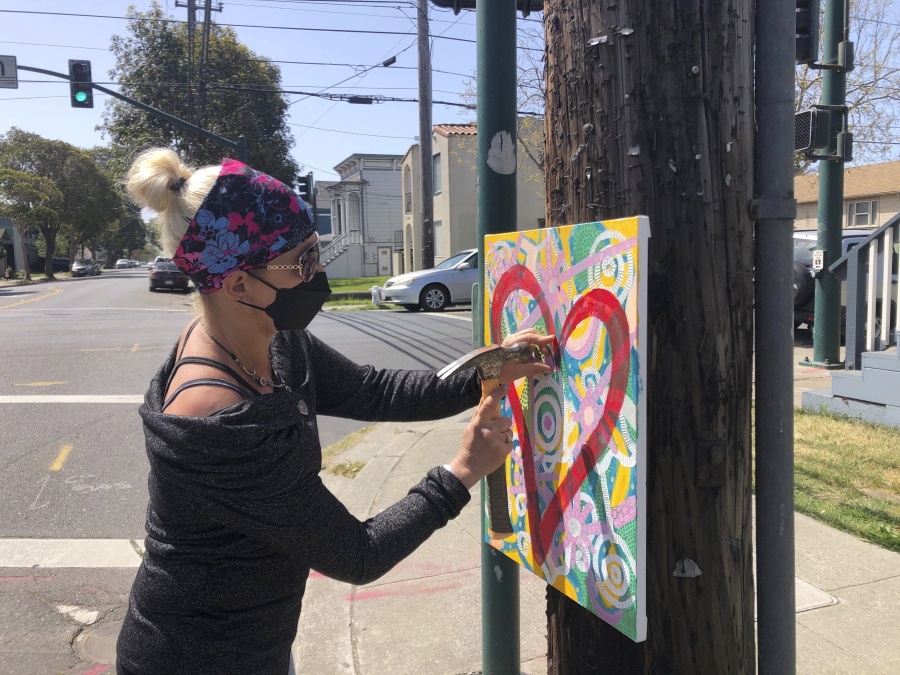 Artist Deirdre Freeman hangs her artwork on a telephone pole in Alameda, Calif., Tuesday, April 13, 2021.