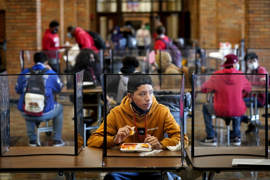 FILE - In this March 31, 2021, file photo, freshman Hugo Bautista eats lunch separated from classmates by plastic dividers at Wyandotte County High School in Kansas City, Kan., on the first day of in-person learning. With a massive infusion of federal aid coming their way, schools across the U.S. are weighing how to use the windfall to ease the harm of the pandemic - and to tackle problems that existed long before the coronavirus.