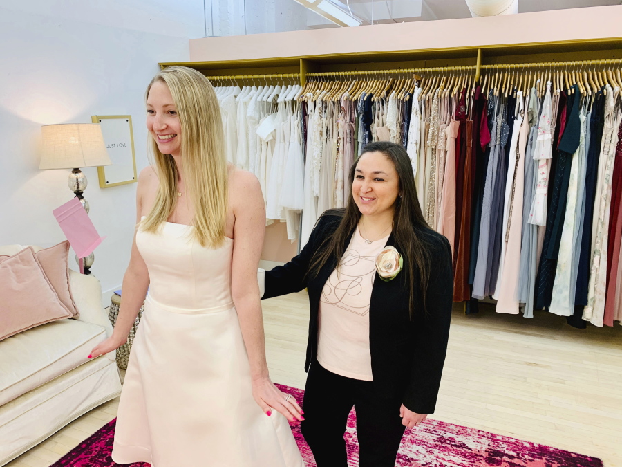 In this photo provided by Gilded Social, a bridal shop in Columbus, Ohio, owner Tanya Rutner Hartman helps customer Cristin Lee try on a gown at the shop on April 2, 2021. Although weddings and other big celebrations are going back on the calendar in the U.S., business owners who make those events happen expect a slow recovery from the impact of COVID-19. Hartman sees a shift in how couples feel about weddings, a change that can affect other businesses in the events industry as well.