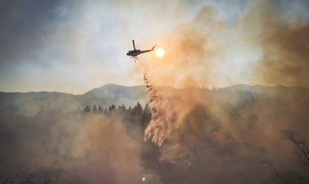 A helicopter with water helps to contain a wildfire.