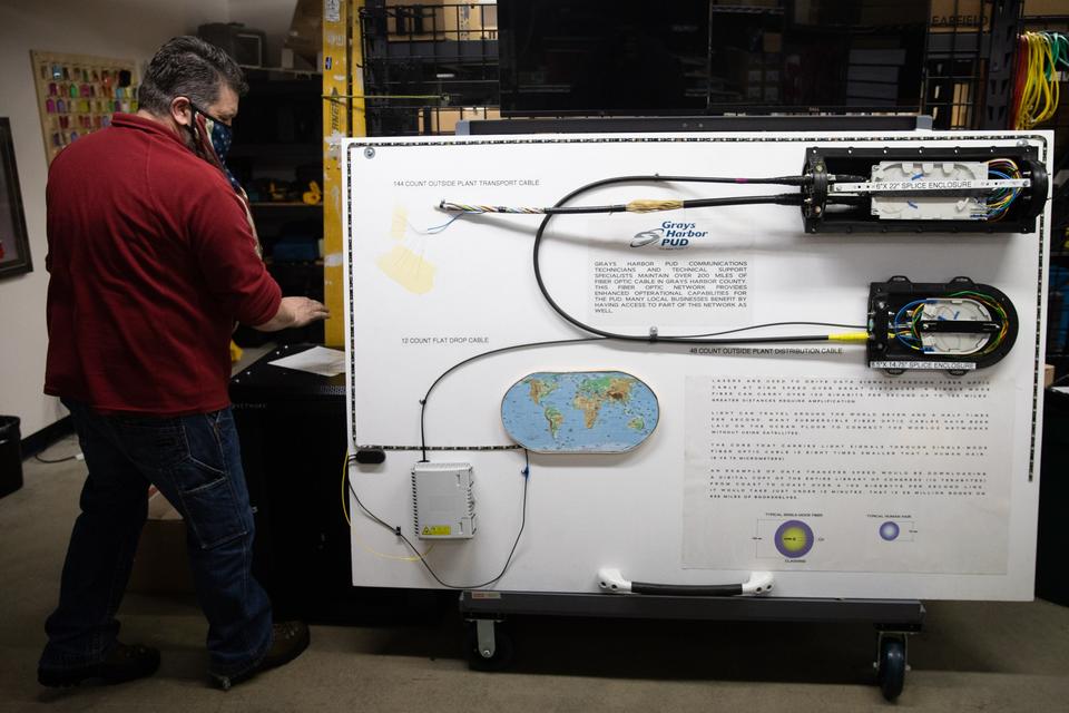 Michael Moore, an information technology construction coordinator, is seen with an explanatory board about telecommunications services at a co-location data center inside Grays Harbor Pubic Utility District's headquarters in Aberdeen on March 4, 2021. Two bills approved by Washington's Legislature would let public utility districts offer broadband to retail customers. But there's some confusion about how the bills would interact. (Matt M.
