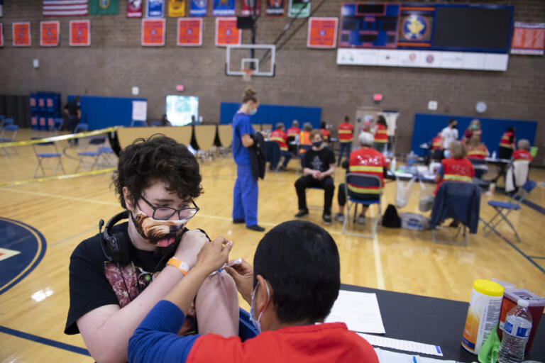 Ridgefield High School sophomore William Lewis, 16, wears a dog-themed mask as he receives his COVID-19 vaccination from pharmacist Estela Clemente in the school's gym on Wednesday morning. The vaccination clinic, which was also open to members of the community, was organized with help from students at the school. Around 300 pre-registered to receive vaccines, according to organizers.