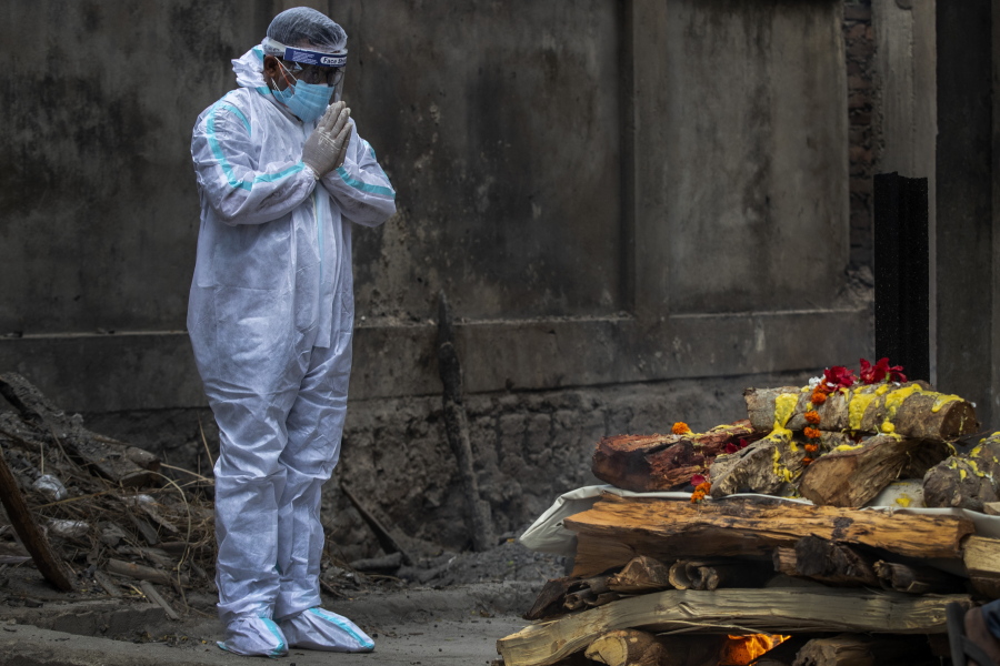 A relative in protective suit performs last rituals as the body of a person who died of COVID-19 is cremated in Gauhati, India, Monday, May 24, 2021. India crossed another grim milestone Monday of more than 300,000 people lost to the coronavirus as a devastating surge of infections appeared to be easing in big cities but was swamping the poorer countryside.