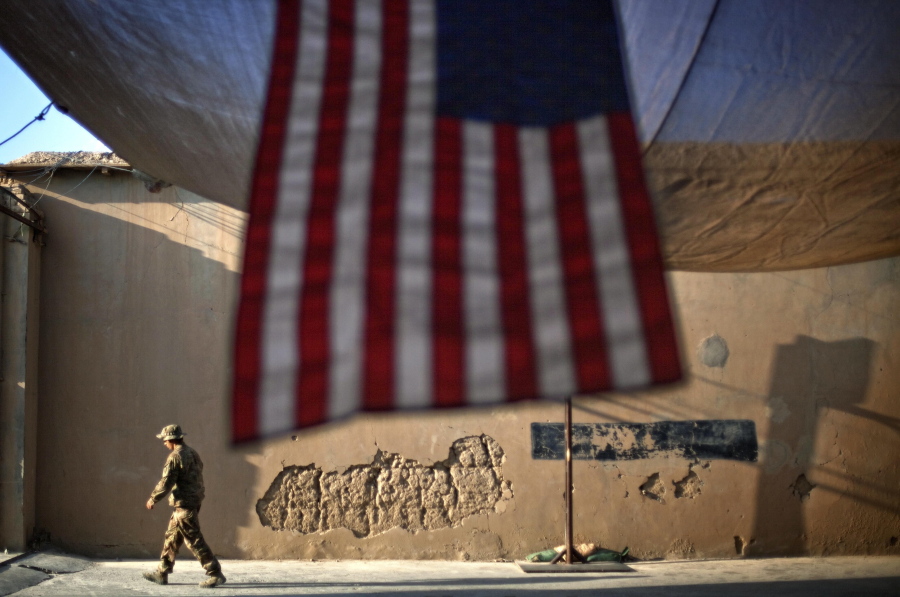FILE - In this Sept. 11, 2011 file photo, a U.S. Army soldier walks past an American Flag hanging in preparation for a ceremony commemorating the tenth anniversary of the 9/11 attacks, at Forward Operating Base Bostick in Kunar province, Afghanistan. The final phase of ending America's "forever war" in Afghanistan after 20 years formally began Saturday, May 1, 2021, with the withdrawal of the last U.S.