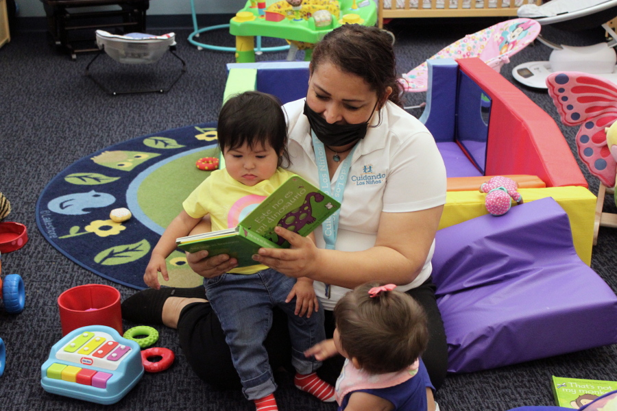 This May 4, 2021 image shows teacher Graciela Olague-Barrios reading to two infants at Cuidando Los Ninos in Albuquerque, N.M. The charity provides housing, child care and financial counseling for mothers, all of whom will benefit from expanded Child Tax Credit payments that will start flowing in July to roughly 39 million households.