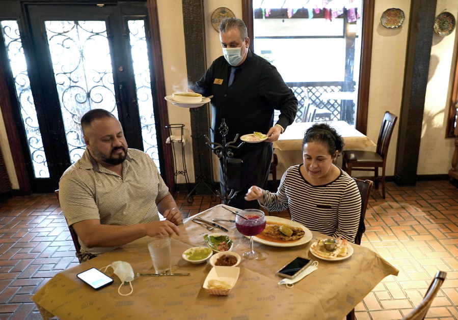 FILE - In this Wednesday, March 10, 2021 file photo, waiter Jose Bravo, center, delivers food for Alberto Castaneda, left, and his wife, Esther, at Picos restaurant in Houston. The Institute for Supply Management, an association of purchasing managers, reported Monday, April 5 that the U.S. services sector, which employs most Americans, recorded record growth in March as orders, hiring and prices all surged.  (AP Photo/David J.