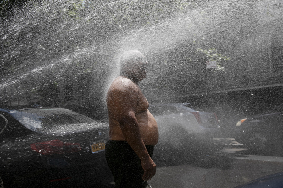 FILE - In this Tuesday, July 28, 2020 file photo, Rey Gomez cools off in the spray from a fire hydrant in New York, as the city opened more than 300 fire hydrants with sprinkler caps to help residents cool off during a heat wave. According to a study published Tuesday, May 25, 2021 in Nature Communications, during the summer of 2017 in nearly all large urban areas, people of color are exposed to more extreme urban heat than white people.