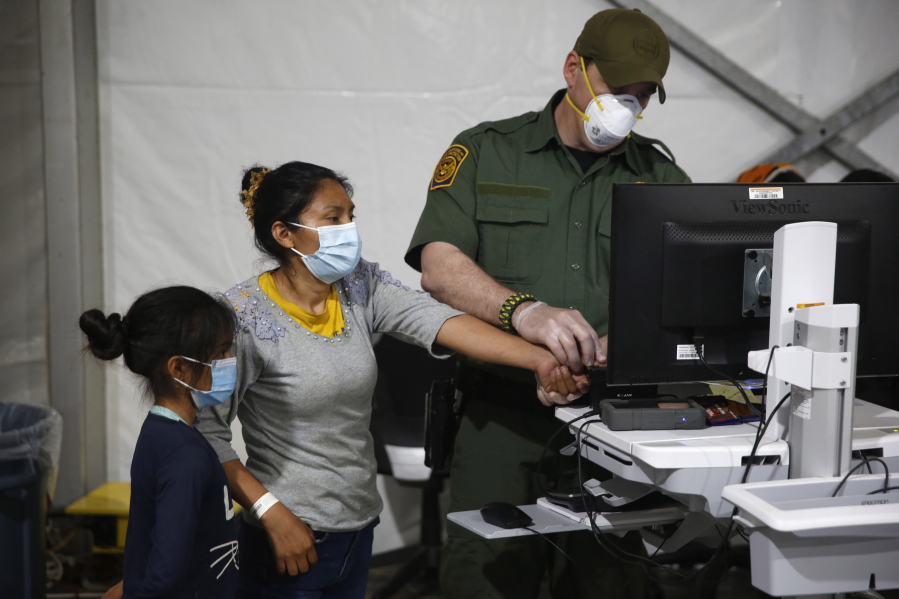 FILE - In this March 30, 2021, file photo, a migrant and her daughter have their biometric data entered at the intake area of the U.S. Department of Homeland Security holding facility, the main detention center for unaccompanied children in the Rio Grande Valley, in Donna, Texas. Migrant families will be held at hotels in the Phoenix area in response to a growing number of people crossing the U.S.-Mexico border, authorities said Friday, April 9, 2021 another step in the Biden administration's rush to set up temporary space for them.