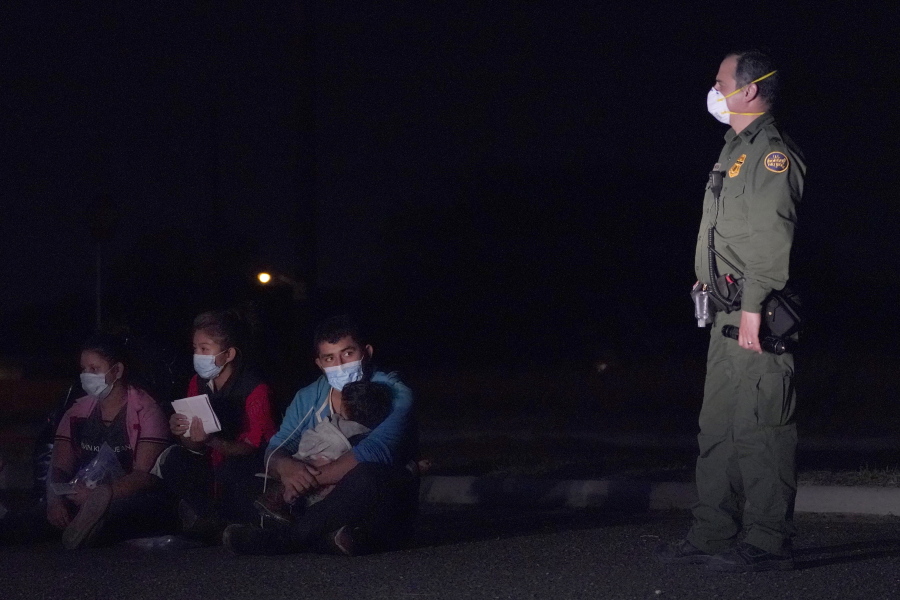 In this March 24, 2021 photo, a migrant man, center, holds a child as he looks at a U.S. Customs and Border Protection agent at an intake area after crossing the U.S.-Mexico border, early Wednesday, March 24, 2021, in Roma, Texas. The Biden administration said Monday that four families that were separated at the Mexico border during Donald Trump's presidency will be reunited in the United States this week in what Homeland Security Secretary Alejandro Mayorkas calls "just the beginning" of a broader effort.