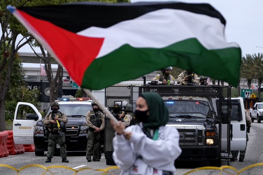 A demonstrator waves the flag of Palestine as police officers guard outside the Federal Building during a protest against Israel and in support of Palestinians, Saturday, May 15, 2021, in the Westwood section of Los Angeles. (AP Photo/Ringo H.W.