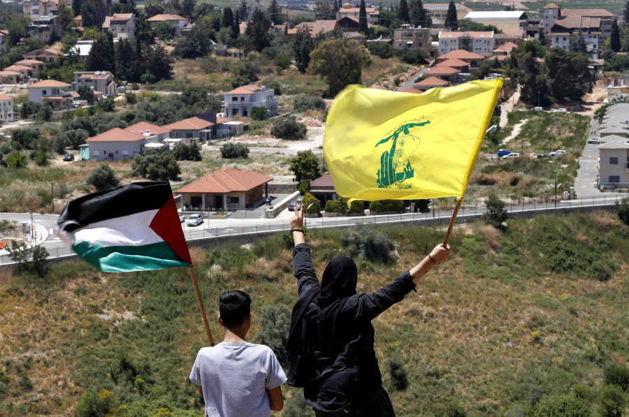 FILE - In this May 15, 2021, file photo, Lebanese wave Hezbollah and Palestinian flags, as they stand in front of the Israeli town of Metula, background, on the Lebanese side of the Lebanese-Israeli border in the southern village of Kfar Kila, Lebanon. Lebanon's Hezbollah militia looms large over the current Israel-Hamas war, even though it has stayed out of the fighting so far. Hezbollah's firepower is far greater than that of Gaza's Hamas rulers, and Israel keeps a wary eye on its northern border for any signs Hezbollah might get off the sidelines.