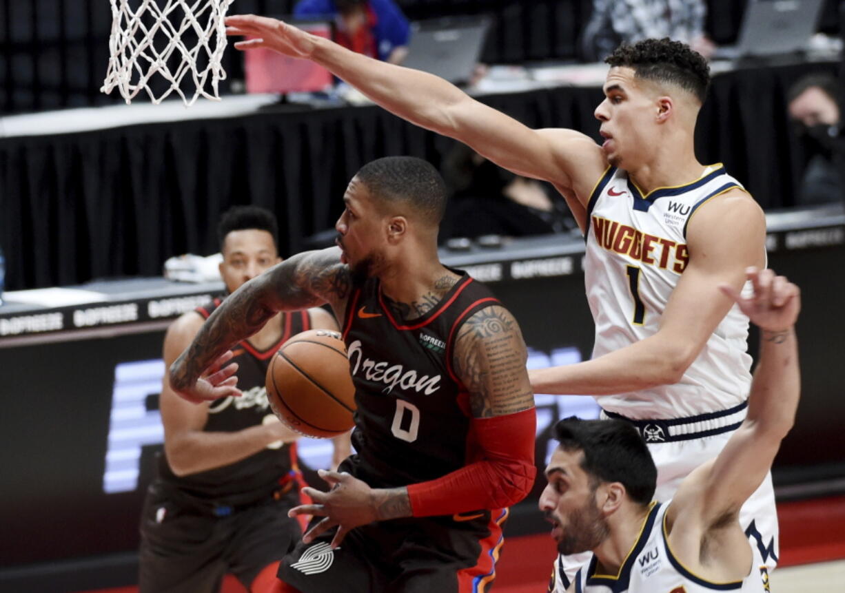 Portland Trail Blazers guard Damian Lillard, center, passes the ball behind his back to guard CJ McCollum, left, as Denver Nuggets forward Michael Porter Jr., right, defends during the first half of an NBA basketball game in Portland, Ore., Sunday, May 16, 2021.
