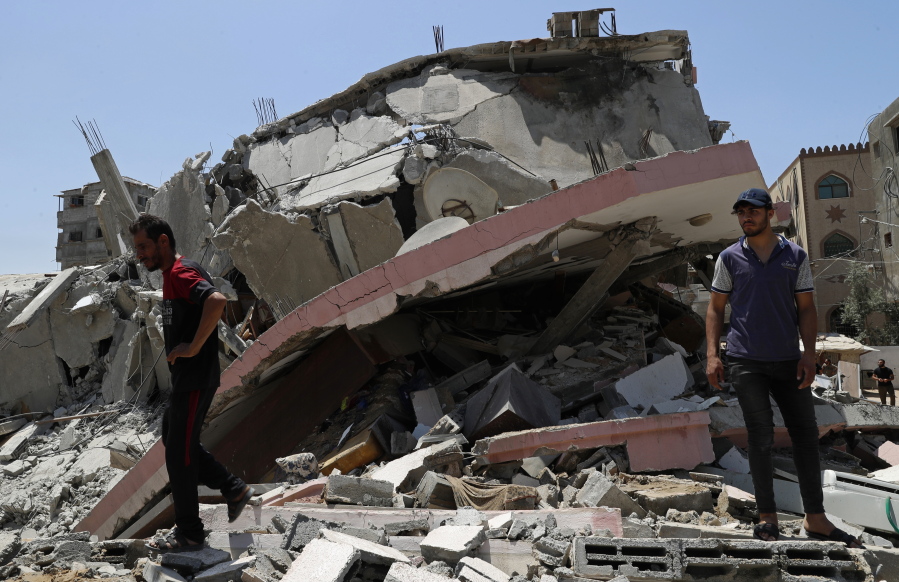 People walk amid the rubble of a destroyed residential building which was hit by Israeli airstrikes, in Gaza City, Wednesday, May 12, 2021.