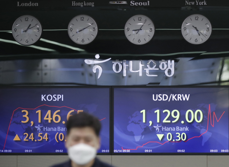 An employee of a bank walks by screens showing the Korea Composite Stock Price Index (KOSPI), left, and the foreign exchange rate between U.S. dollar and South Korean won at the foreign exchange dealing room in Seoul, South Korea, Friday, May 14, 2021. Asian shares rose Friday after Wall Street put the brakes on a three-day losing streak with a broad stock market rally powered by Big Tech companies and banks.