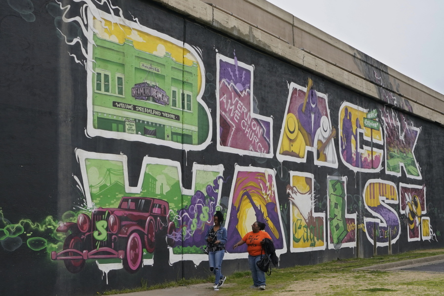 Javohn Perry, left, of Seattle, and her cousin, Danielle Johnson, right, of Beggs, Okla., walk past the Black Wall Street mural Monday, April 12, 2021, in Tulsa, Okla. The original Black Wall Street vaporized a hundred years ago, when a murderous white mob laid waste to what was the nation's most prosperous Black-owned business district and residential neighborhood.