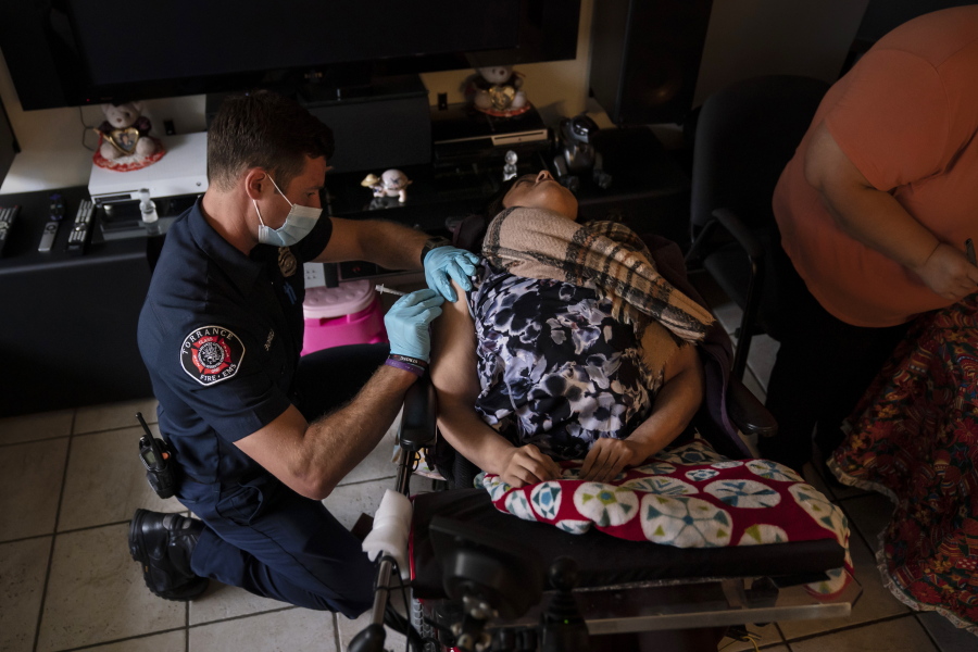 Torrance firefighter Trevor Borello, left, administers the second dose of the Pfizer COVID-19 vaccine to Barbara Franco, who suffers from muscular dystrophy, at her apartment, Wednesday, May 12, 2021, in Torrance, Calif. Teamed up with the Torrance Fire Department, Torrance Memorial Medical Center started inoculating people at home in March, identifying people through a city hotline, county health department, senior centers and doctor's offices, said Mei Tsai, the pharmacist who coordinates the program. (AP Photo/Jae C.