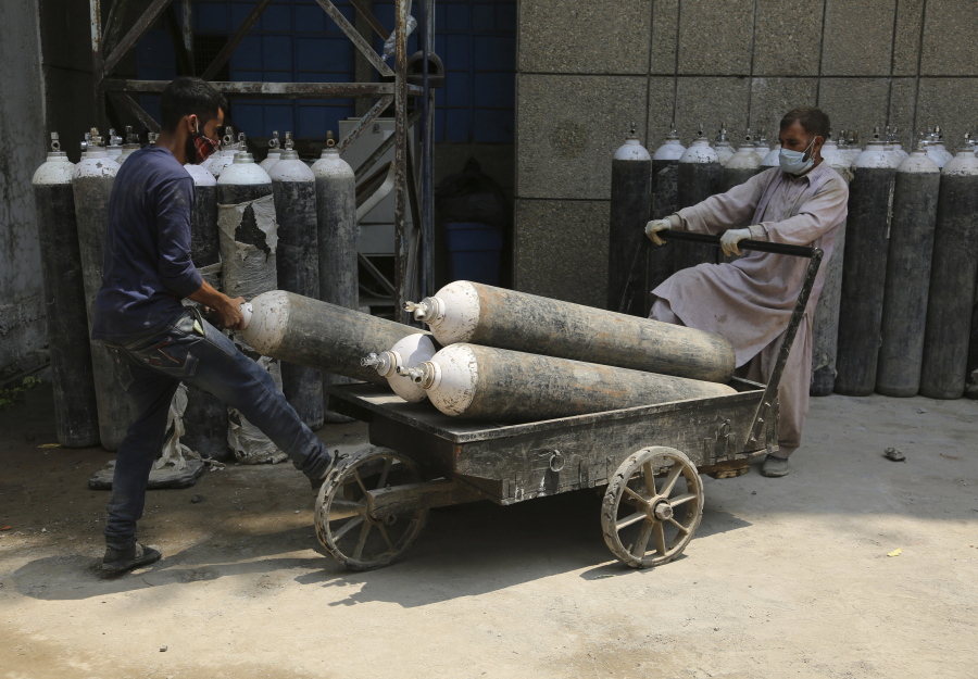 Workers load oxygen cylinders onto a hand cart to be carried inside the COVID-19 wards at a government run hospital in Jammu, India, Friday, May 7, 2021. With coronavirus cases surging to record levels, Indian Prime Minister Narendra Modi is facing growing pressure to impose a harsh nationwide lockdown amid a debate whether restrictions imposed by individual states are enough.