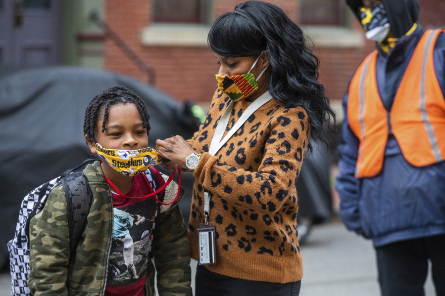 FILE - In this Monday, March 29, 2021, file photo, Jenea Edwards, of the North Side, helps her son Elijah, 9, in the third grade, with his mask before heading into Manchester Academic Charter School on the first day of in-person learning via a hybrid schedule, in Pittsburgh. Dozens of school districts around the country have eliminated requirements for students to wear masks, and many more are likely to ditch mask requirements before the next academic year.