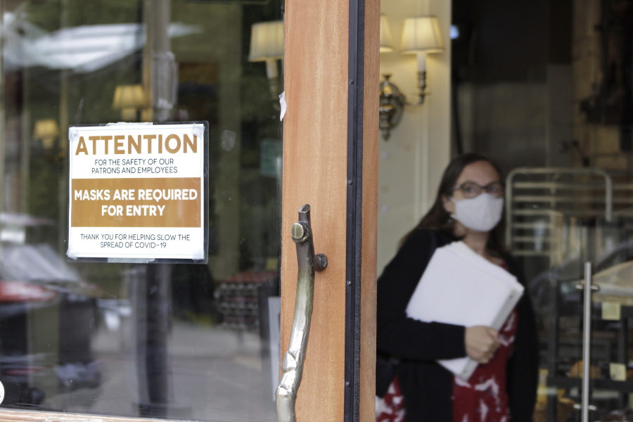 A sign reminds customers to wear their masks at a bakery in Lake Oswego, Ore., on Friday, May 21, 2021. As the federal government and many states ease rules around mask-wearing and business occupancy, some blue states like Oregon and Washington are still holding on to some longtime coronavirus restrictions.
