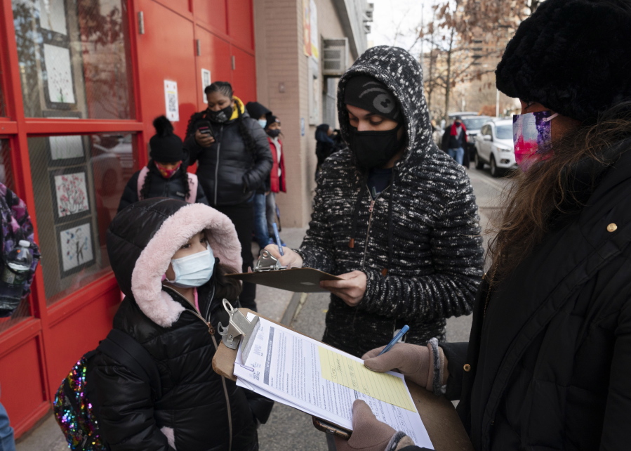 FILE - In this Dec. 7, 2020, file photo, a parent, center, completes a form granting permission for random COVID-19 testing for students as he arrives with his daughter, left, at P.S. 134 Henrietta Szold Elementary School, in New York. Children are having their noses swabbed or saliva sampled at school to test for the coronavirus in cities such as Baltimore, New York and Chicago. As more children return to school buildings this spring, widely varying approaches have emerged on how and whether to test students and staff members for the virus.
