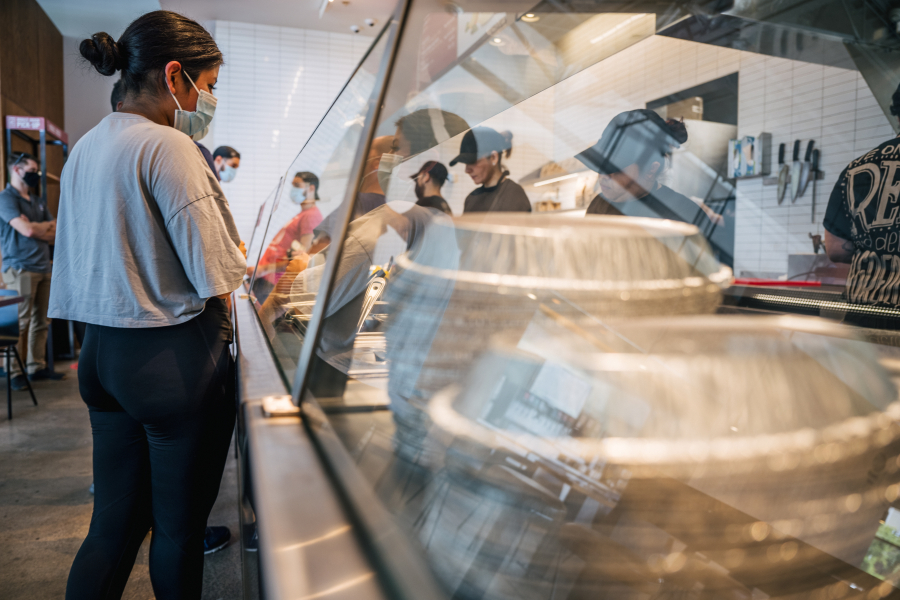 A woman waits in line for food at a Chipotle Mexican Grill  on June 9, 2021 in Houston, Texas. Menu prices at the Chipotle Mexican Grill have risen by roughly 4% to cover the costs of raising its' minimum wage to $15 an hour for employees. The restaurant industry has been boosting wages in the hopes of attracting workers during a labor crunch.
