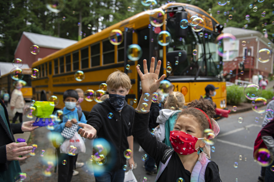 Students including first-grader Trulee Dunn, right, get a warm goodbye from teachers as they prepare to board the bus on the last day of class at Green Mountain School on Tuesday morning. It is tradition for teachers and staff to blow bubbles to bid farewell to the children but this year a bubble machine was used as well.