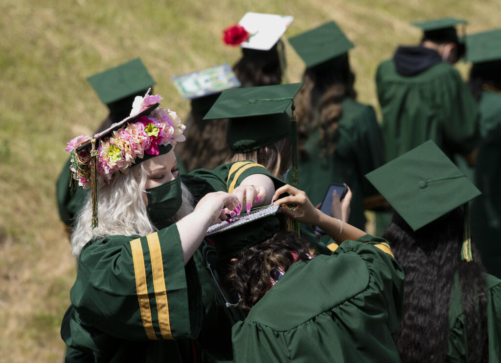 A graduate helps her friend fix the decorations on her graduation cap at the Evergreen High School graduation ceremony on Saturday, June 12, at McKenzie Stadium.