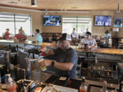 Bartender Mike Dunning of Main Event Sports Grill in east Vancouver pours drinks for customers while working behind the bar on Wednesday afternoon. Statewide pandemic restrictions ended on Wednesday, allowing restaurants and bars to reopen their bar counter seating areas for the first time in more than a year.