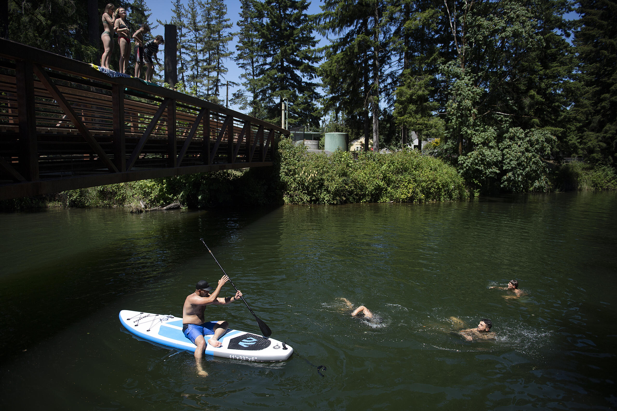 Swimmers join a stand-up paddleboarder as they gather to beat the extreme heat at Lacamas Park on Monday afternoon, June 28, 2021.