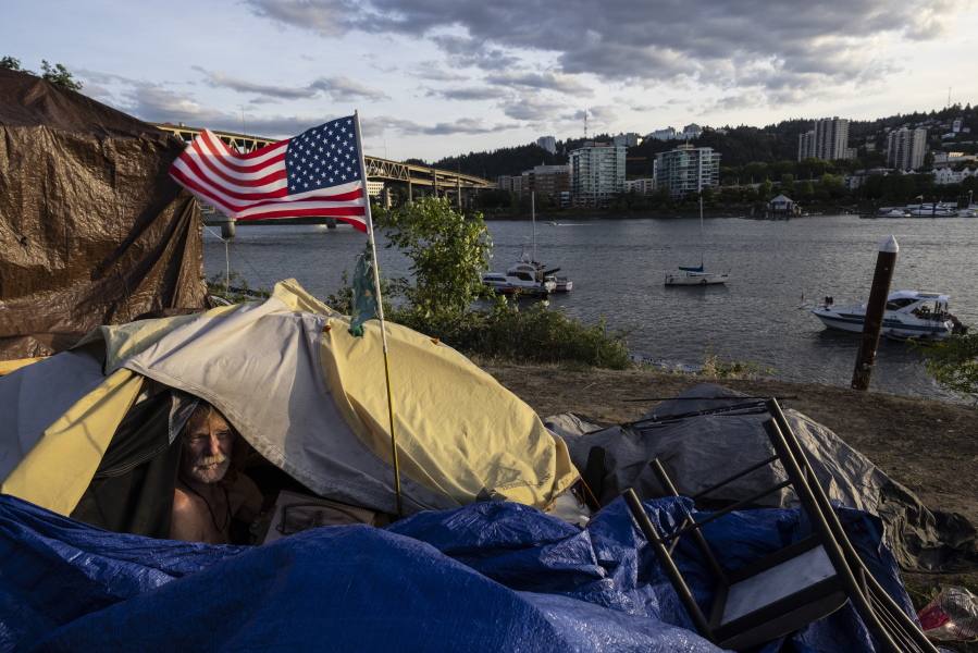 Frank, a homeless man sits in his tent with a river view in Portland, Ore., on Saturday, June 5, 2021. Until a year ago, the city was best known nationally for its ambrosial food scene, craft breweries and "Portlandia" hipsters. Now, months-long protests following the killing of George Floyd, a surge in deadly gun violence, and an increasingly visible homeless population have many questioning whether Oregon's largest city can recover.
