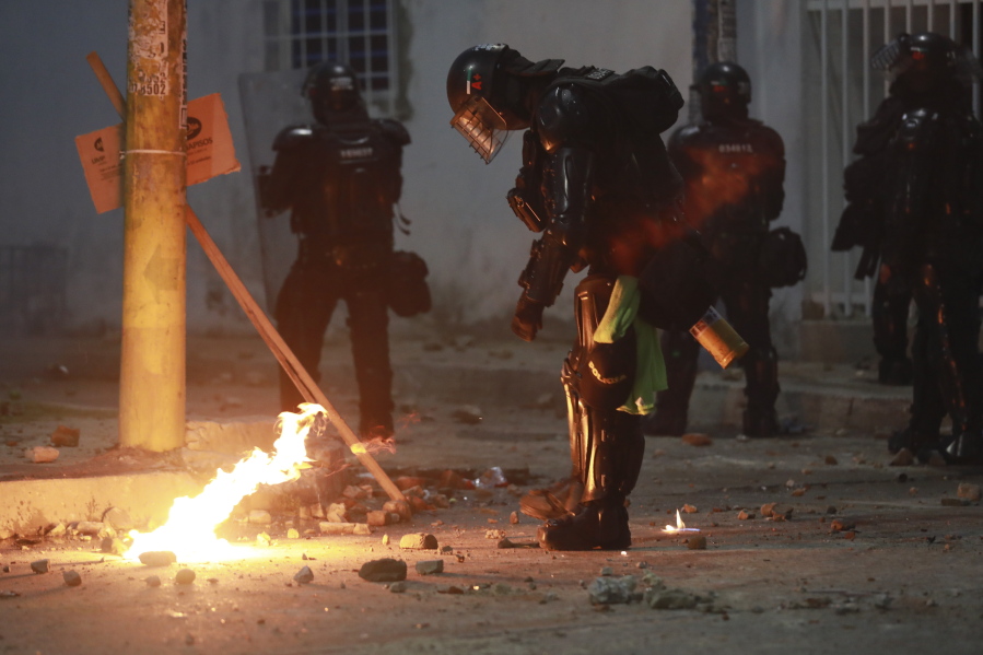Riot police put out a petrol bomb hurdled during clashes with anti-government demonstrators protesting against the FIFA World Cup Qatar 2022 qualifying soccer match between Argentina and Colombia near the Metropolitano stadium in Barranquilla, Colombia, Tuesday, June 8, 2021.