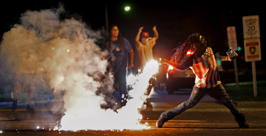 FILE - In this Aug. 13, 2014, file photo Edward Crawford Jr., returns a tear gas canister fired by police who were trying to disperse protesters in Ferguson, Mo. Three journalists with Al Jazeera America who were tear-gassed during a protest in Ferguson, after Michael Brown's death in 2014 have settled a lawsuit with the county whose SWAT team fired the tear gas. St. Charles County agreed to pay $280,000, according to the law firm that represented the journalists.(Robert Cohen/St.