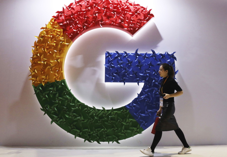 FILE - In this Monday, Nov. 5, 2018 file photo, a woman walks past the logo for Google at the China International Import Expo in Shanghai. France's anti-competition watchdog has decided to fine Google 220 million euros ($268 million) for abusing its "dominant position" in the complex business of online advertising. It said Monday, June 7, 2021 that the move is unprecedented.