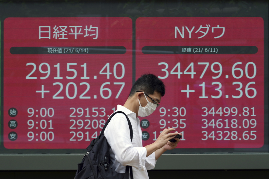 A man wearing a protective mask walks in front of an electronic stock board showing Japan's Nikkei 225 and New York Dow indexes at a securities firm Monday, June 14, 2021, in Tokyo. Asian stock markets were mixed Monday as investors looked ahead to this week's Federal Reserve meeting for hints of possible changes in ultra-low interest rates and other economic stimulus.