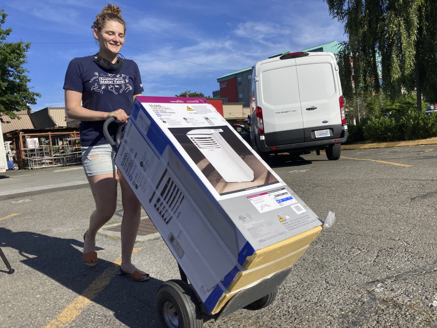 Sarah O'Sell transports her new air conditioning unit to her nearby apartment on a dolly in Seattle on Friday, June 25, 2021. O'Sell snagged one of the few AC units available at the Junction True Value Hardware as Pacific Northwest residents brace for an unprecedented heat wave that has temperatures forecasted in triple-digits.