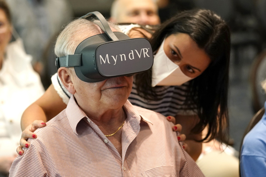 Gloria Gantes, right, monitors Terry Colli, a resident of John Knox Village, as he participates in a virtual reality study, Tuesday, June 1, 2021, in Pompano Beach, Fla. The senior community is in partnership with Stanford University's Virtual Human Interaction Lab on a study to see how older adults respond to virtual reality and whether it can improve their sense of wellbeing.