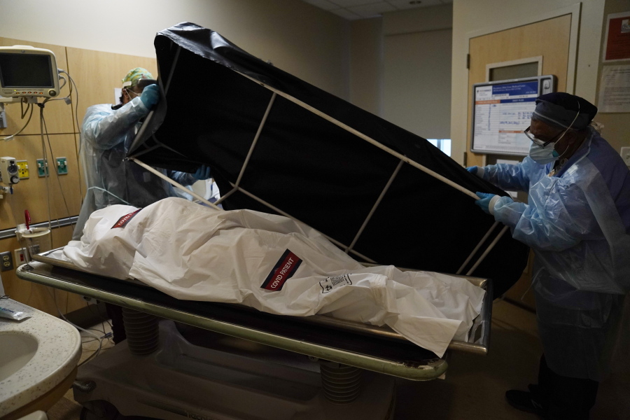 FILE - In this Jan. 9, 2021 file photo, transporters Miguel Lopez, right, Noe Meza prepare to move a body of a COVID-19 victim to a morgue at Providence Holy Cross Medical Center in the Mission Hills section of Los Angeles. The U.S. death toll from COVID-19 has topped 600,000, even as the vaccination drive has drastically slashed daily cases and deaths and allowed the country to emerge from the gloom. (AP Photo/Jae C.
