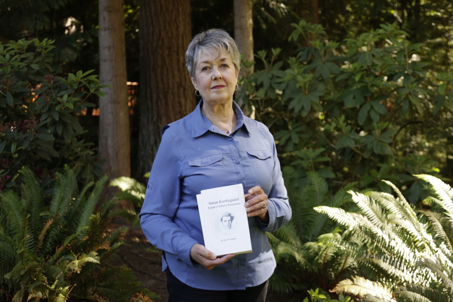 Karen McKnight stands in her backyard on Saturday, June 19, 2021, in Sammamish, Wash., holding two books written by her brother Ross Bagne of Cheyenne, Wyo.