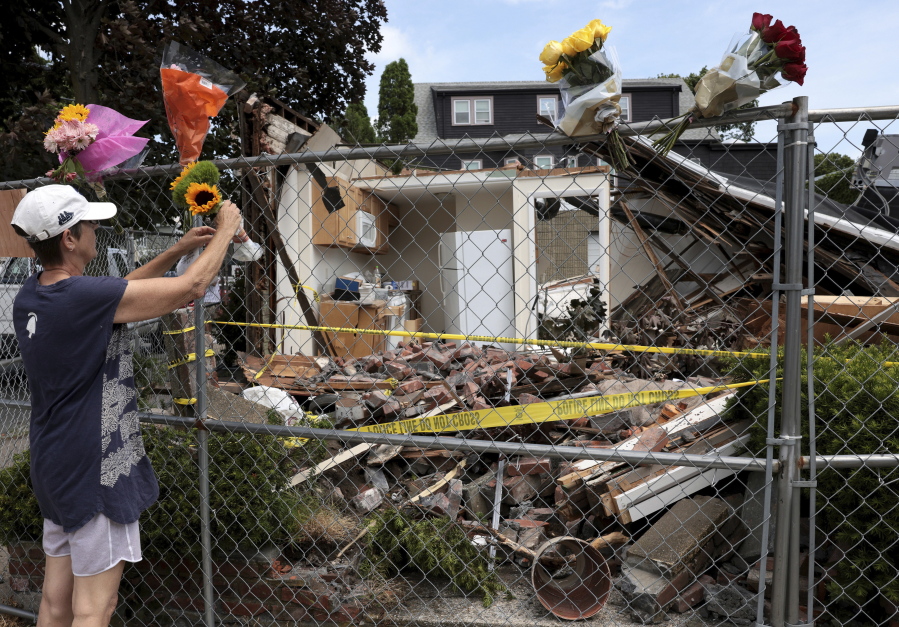In this Sunday, June 27, 2021 photo, a neighbor places a bouquet of flowers on a fence outside of a building in Winthrop, Mass., where an armed man crashed a hijacked truck on Saturday, then fatally shot two bystanders before being killed by police.