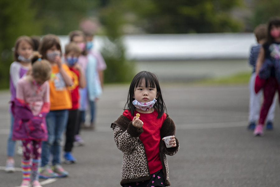 Kindergartner Tiffany Chang briefly drops her mask to enjoy a socially-distanced snack after recess at Eisenhower Elementary School in May. All students and staff will need to wear masks when the school year starts.