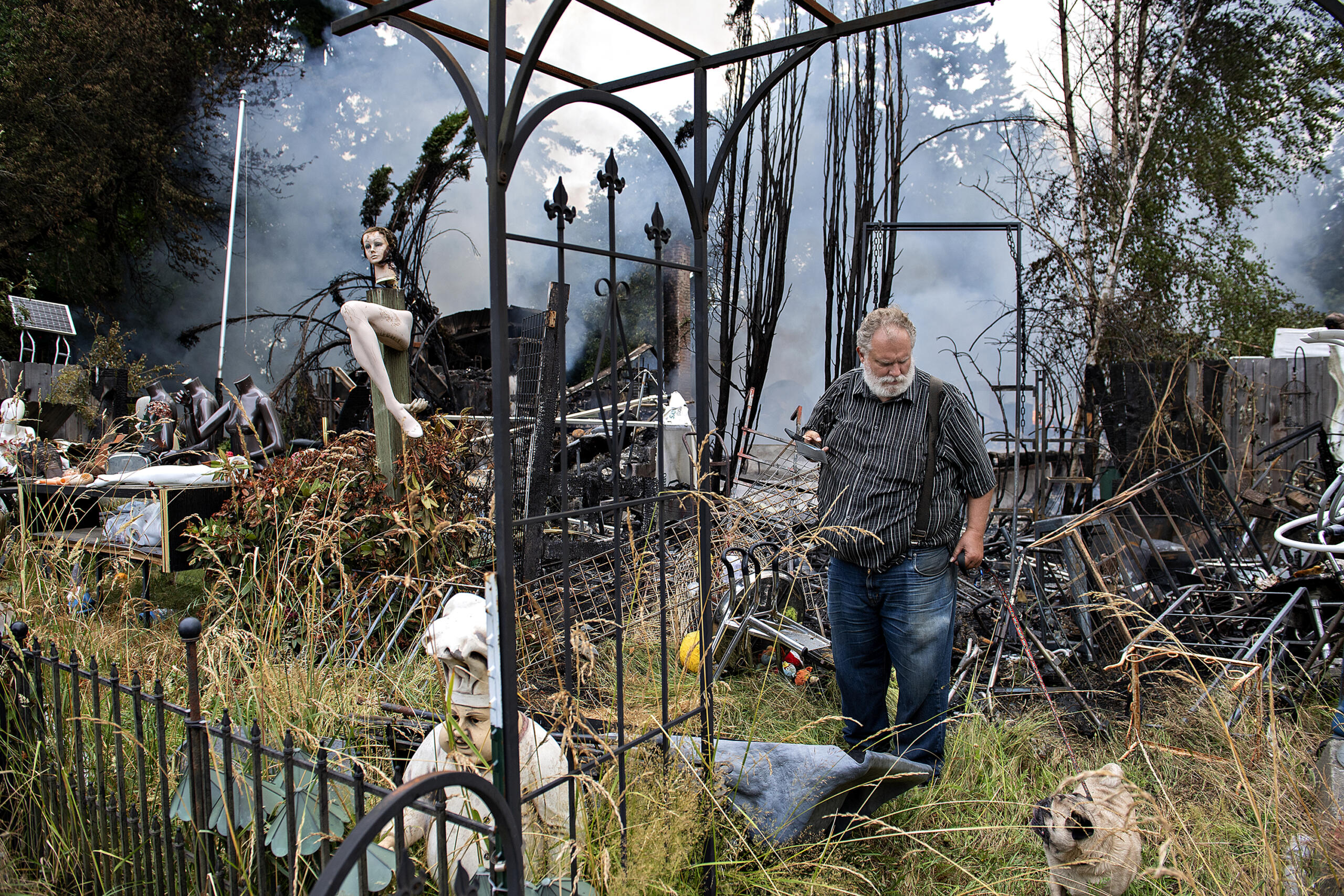 Property owner Steve Slocum surveys the fire scene with his dog, Frank, after a former church and the house next door burned down in an early morning blaze in Battle Ground on Monday, July 5, 2021. Officials said the fire could've been sparked by fireworks and no injuries were reported.