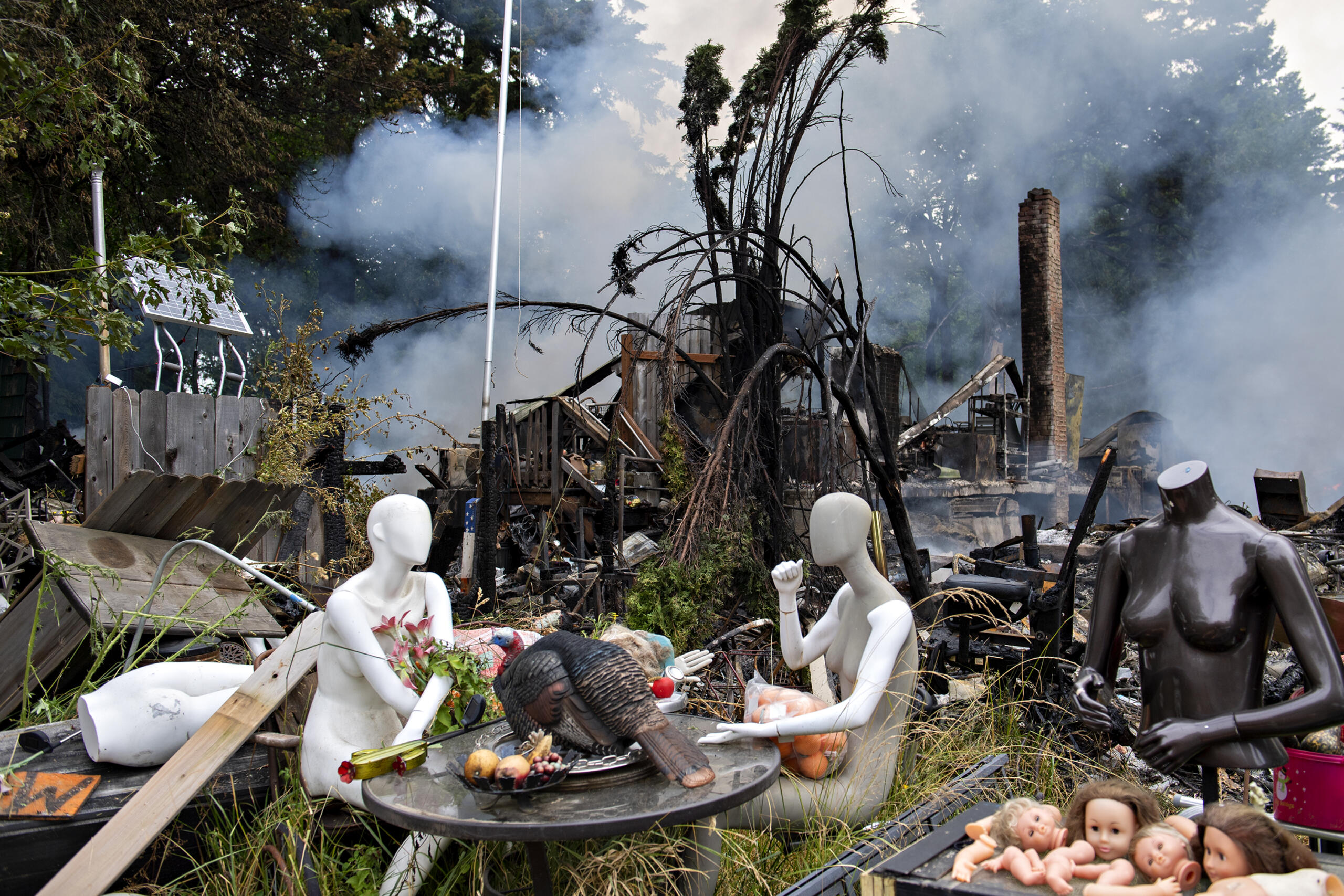 Mannequins sit down to a turkey dinner as the property behind them smolders after an early morning fire on Northeast 92nd Avenue in Battle Ground on Monday morning, July 5, 2021.