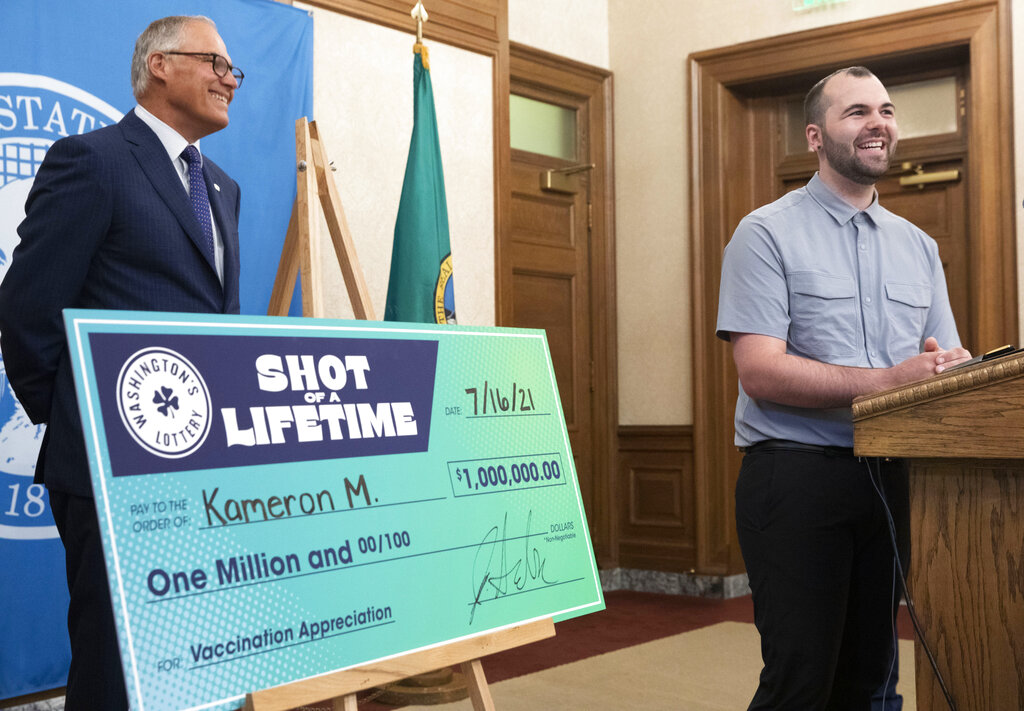 Kameron M., 23, from South King County smiles at a news conference in Olympia, Wash., Friday, July 16, 2021, with Washington Gov. Jay Inslee, left, after accepting a mock check for $1 million, which he won as part of a "Shot of a Lifetime" lottery open to all who got the COVID-19 vaccine. The motorcycle mechanic didn't know about the lottery but said he got his vaccine as soon as he could because he thought it was the right thing to do. Washington is among several states that created lotteries in hopes of increasing the pace of vaccination. (Ellen M.