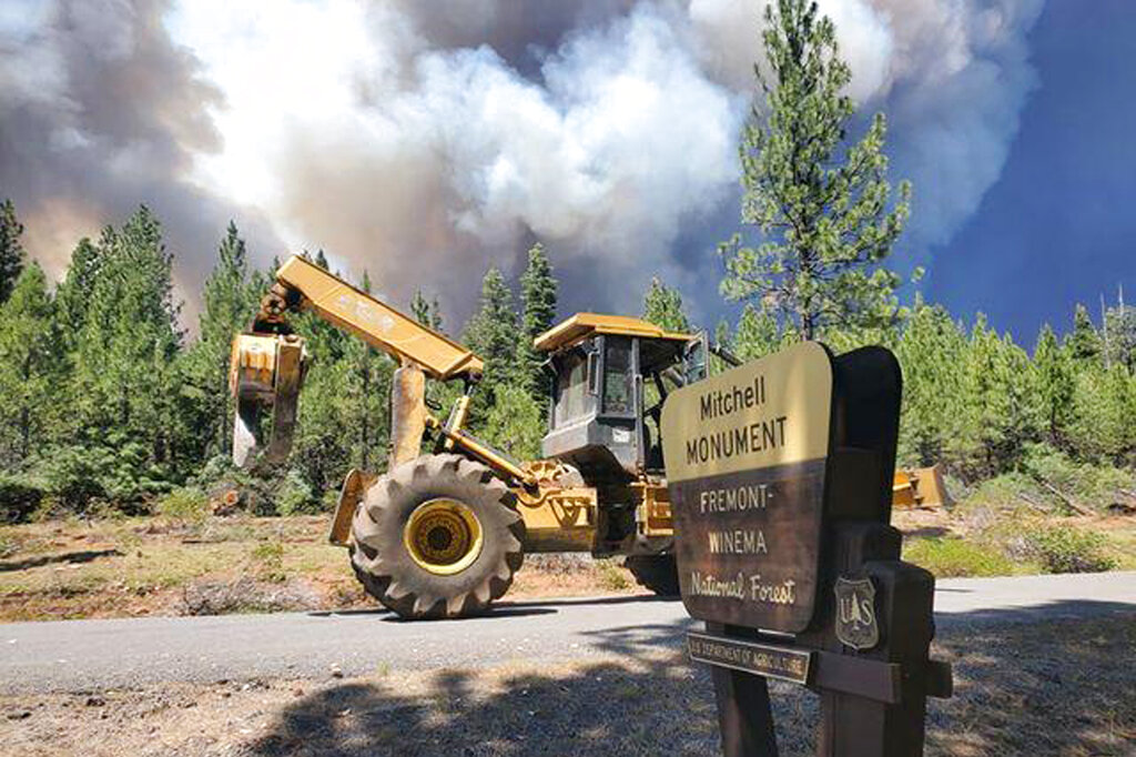 In this photo provided by the Bootleg Fire Incident Command, the Bootleg Fire burns behind heavy equipment at the Mitchell Monument in southern Oregon on Saturday, July 17, 2021. The 569-square-mile (1,474 square kilometers) Bootleg Fire is burning 300 miles (483 kilometers) southeast of Portland in and around the Fremont-Winema National Forest, a vast expanse of old-growth forest, lakes and wildlife refuges.