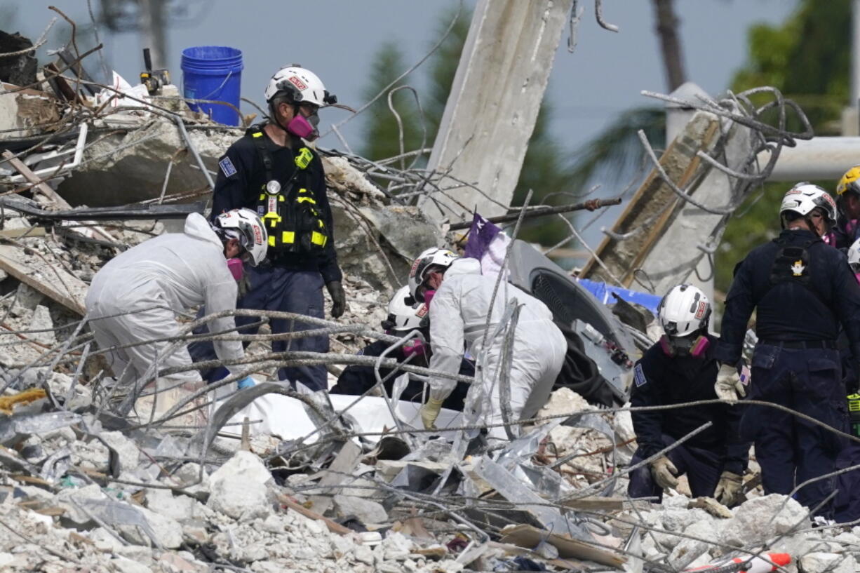 Rescue workers handle a tarp containing recovered remains at the site of the collapsed Champlain Towers South condo building, Monday, July 5, 2021, in Surfside, Fla. The remaining structure was demolished Sunday, which partially collapsed June 24. Many people remain unaccounted for.