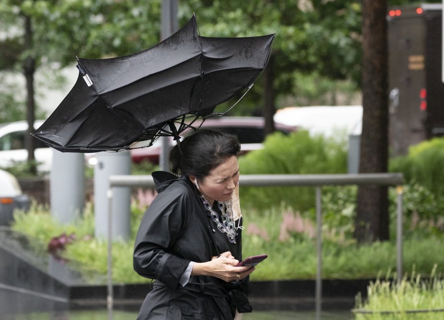 A woman's umbrella is flipped inside out as she walks on a rainy and windy New York street, Friday, July 9, 2021. Fast-moving Tropical Storm Elsa hit the New York City region with torrential rains and high winds as it churned up the East Coast.