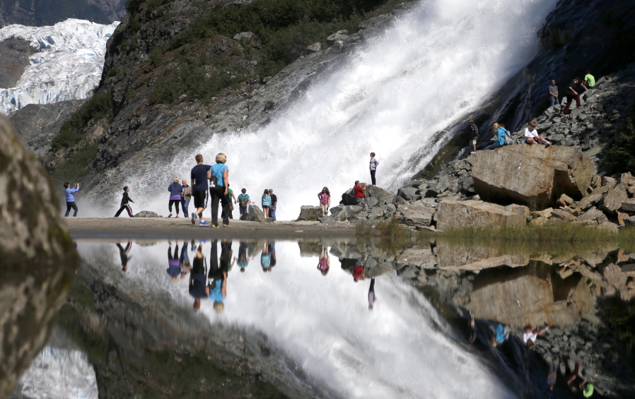 FILE - In this July 31, 2013, file photo, tourists visiting the Mendenhall Glacier in the Tongass National Forest are reflected in a pool of water as they make their way to Nugget Falls in Juneau, Alaska. The Biden administration said Thursday, July 15, 2021, that it is ending large-scale, old-growth timber sales on the nation's largest national forest, the Tongass National Forest in Alaska, and will instead focus on forest restoration, recreation and other non-commercial uses.